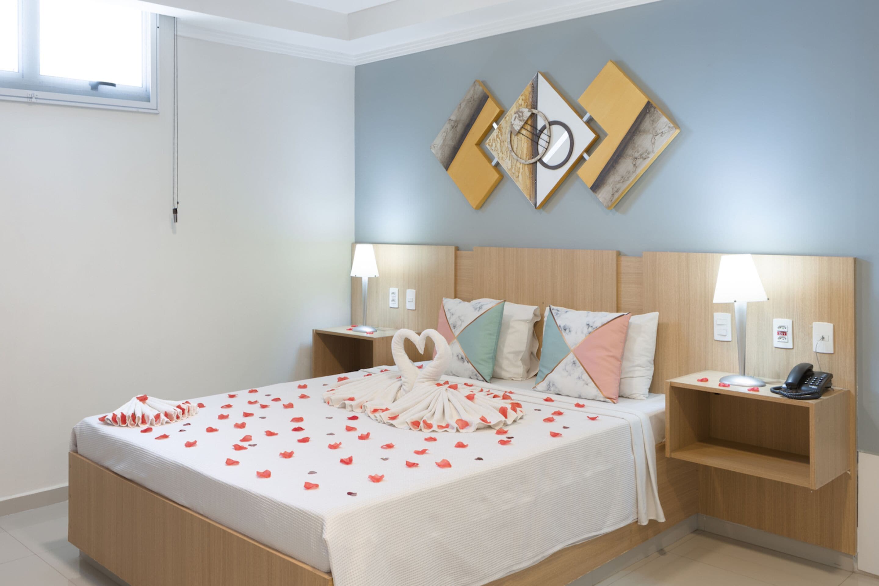 A neatly made bed with a heart-shaped centerpiece, two bedside tables with lamps, and a wall with abstract art.