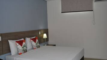 A hotel room with a bed, a nightstand, a lamp, and a window with a blind.