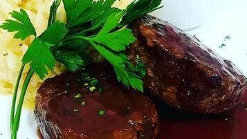 Um prato com duas almôndegas, purê de batata e um toque de salsa.