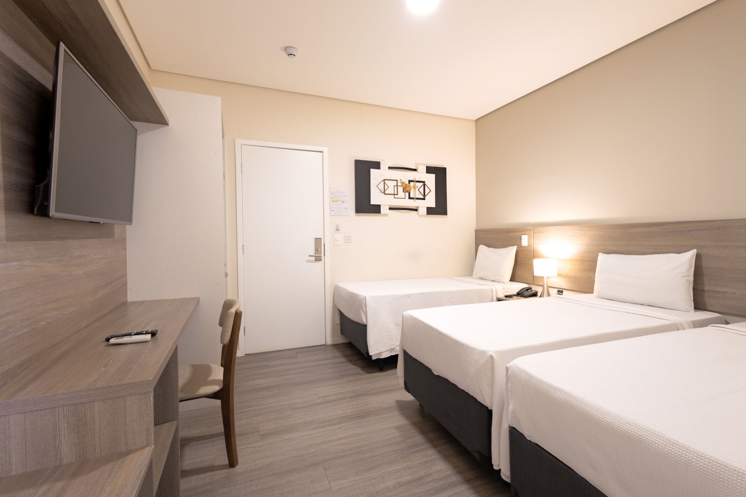 A hotel room with two beds, a desk, a chair, a TV, and a wall-mounted artwork.