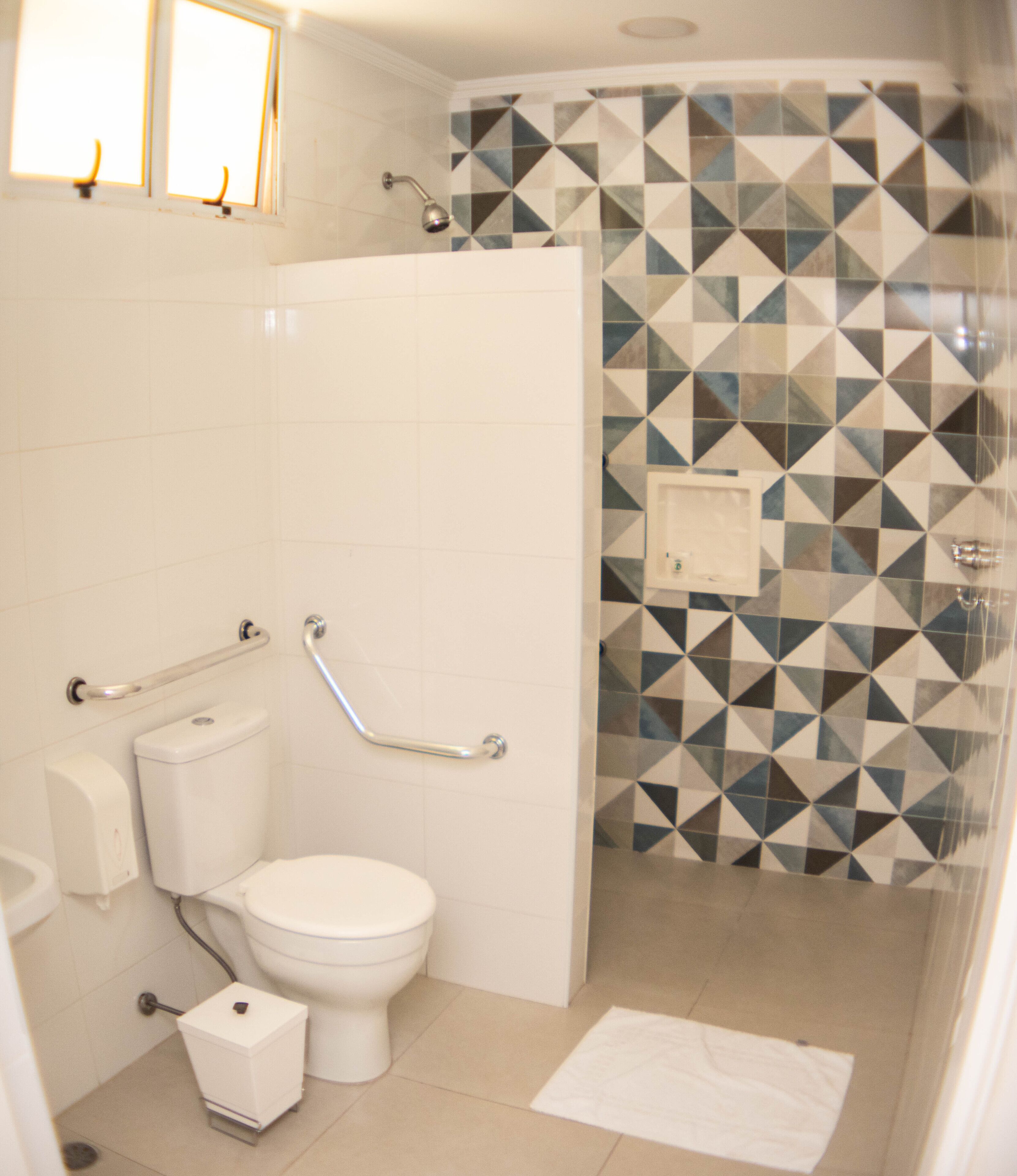 Et badeværelse med toilet, gelændere, bruser og flisebeklædt væg.