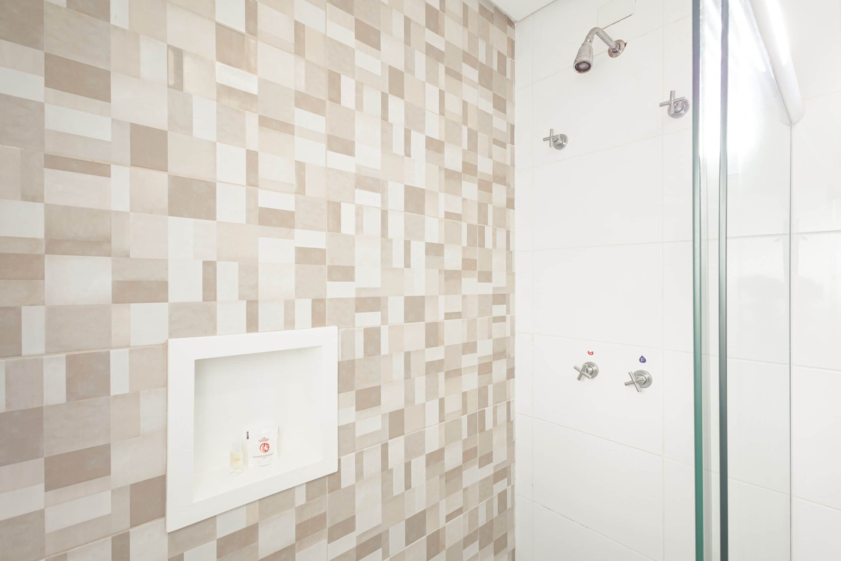 Un baño con pared de azulejos, cabina de ducha con mampara de vidrio y estante blanco con artículos de aseo.