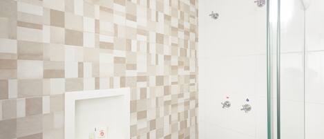 Un baño con pared de azulejos, cabina de ducha con mampara de vidrio y estante blanco con artículos de aseo.