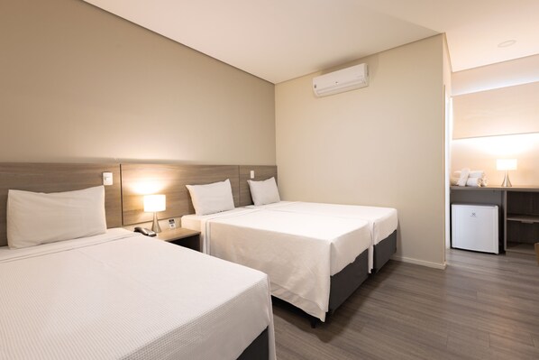 Habitación de hotel con dos camas individuales, un escritorio con silla, un refrigerador pequeño y aire acondicionado de pared.
