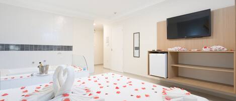 Habitación de hotel con cama, televisión, minibar y zona de ducha.