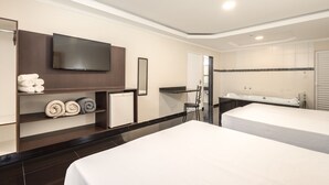 Une chambre d’hôtel avec deux lits, un téléviseur fixé au mur, une salle de bain avec une baignoire et un lavabo, et une étagère avec des serviettes.