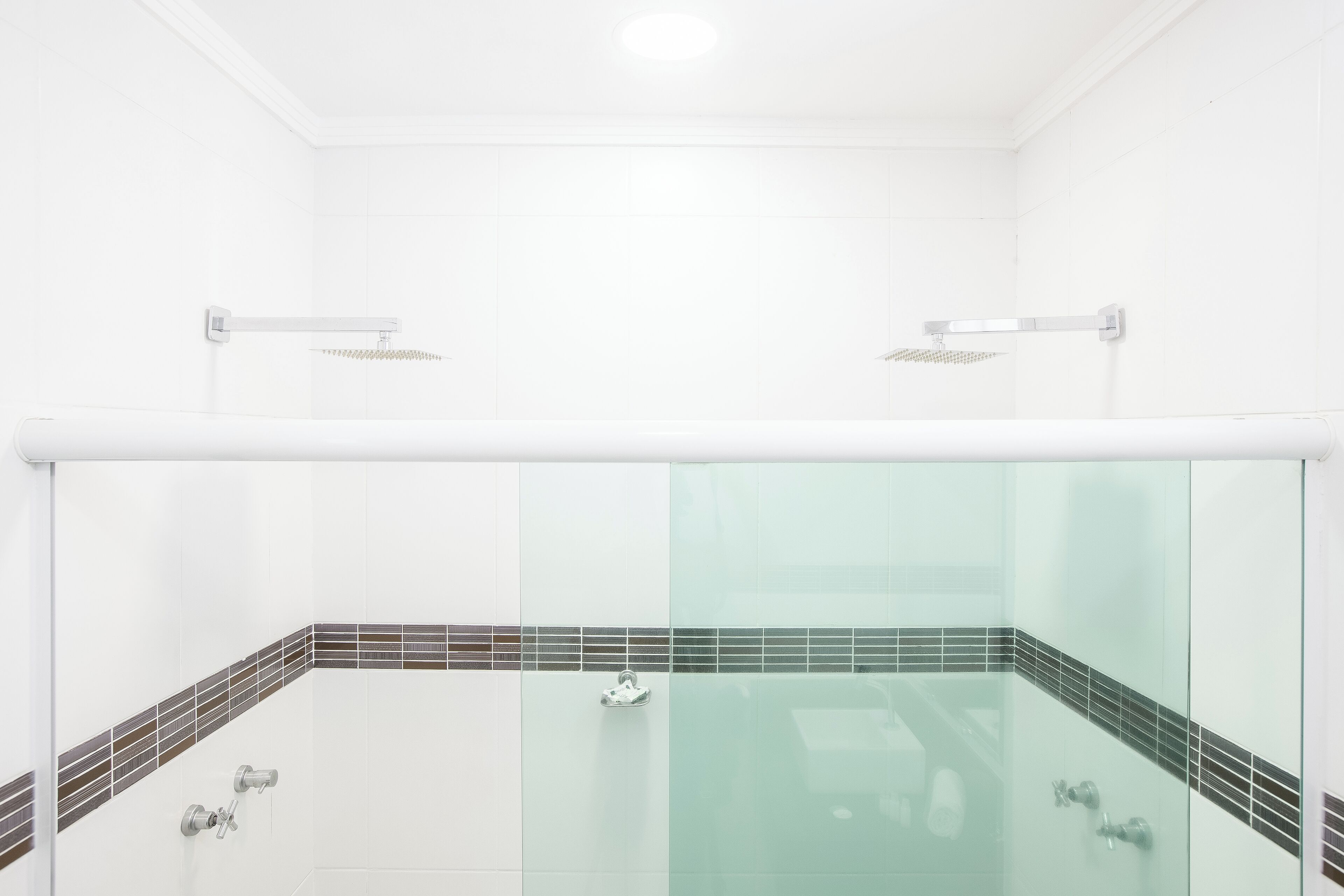 Un baño moderno con ducha de vidrio, azulejos blancos y un espejo pequeño.