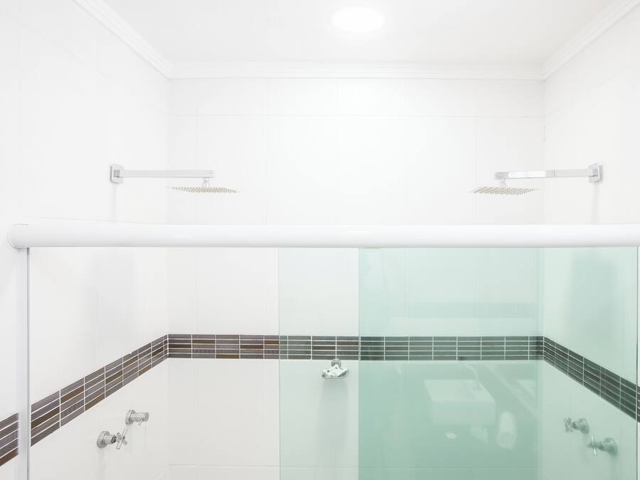 A modern bathroom with a glass-enclosed shower, white tiles, and a small mirror.