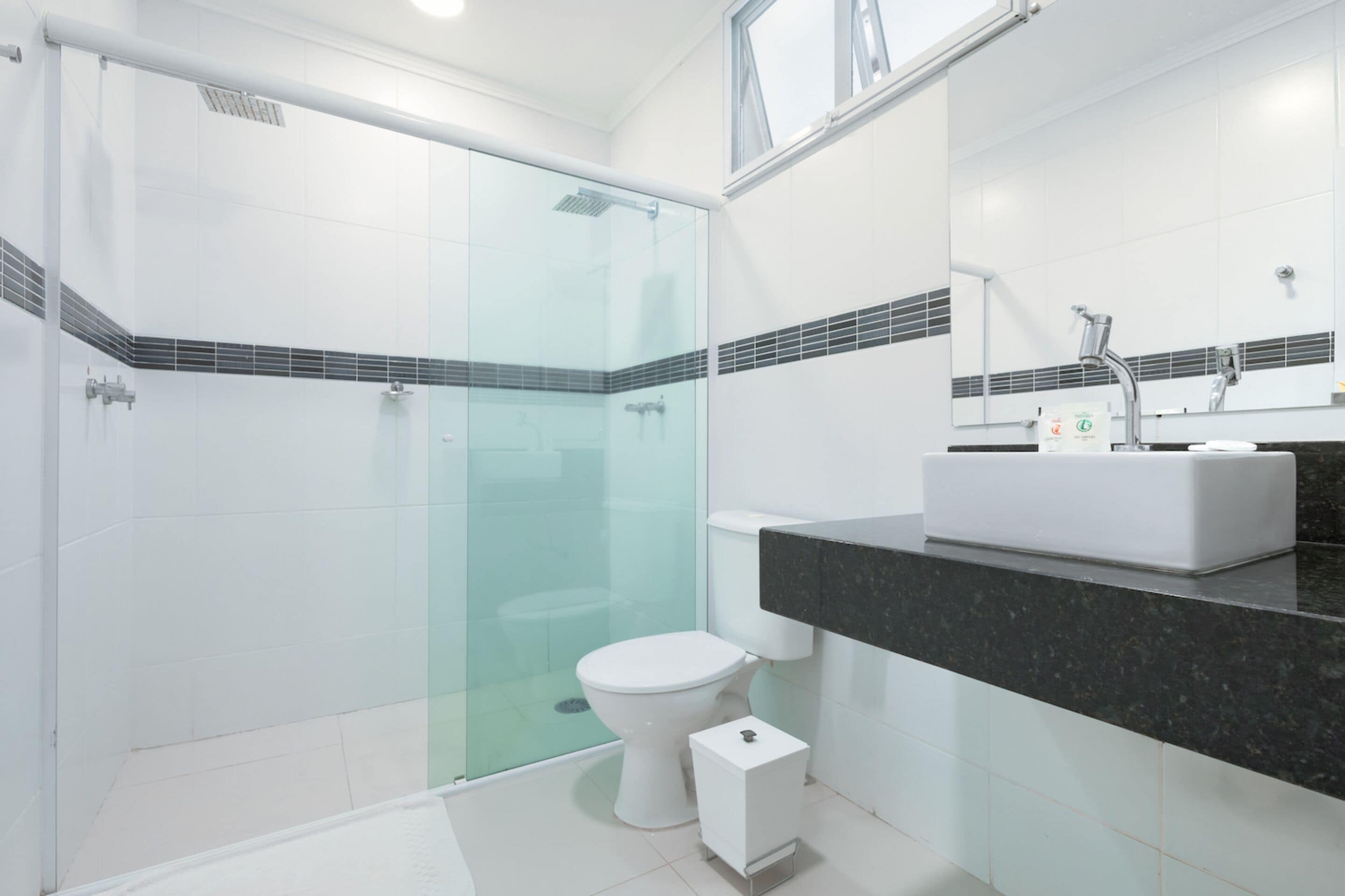 Un baño moderno con ducha de vidrio, inodoro blanco y encimera negra con lavamanos.