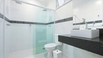 Un baño moderno con ducha de vidrio, inodoro blanco y encimera negra con lavamanos.