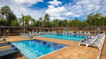 Piscina com espreguiçadeiras e guarda-sóis, cercada por palmeiras e um céu claro.