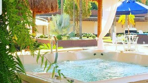 Un espace avec un jacuzzi, doté d’un toit de chaume, entouré de verdure et situé au bord de la piscine.