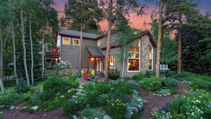 A two-story house with a stone exterior, surrounded by a lush garden and tall trees. - Foxtail Gardens  | Heart of Breck | View | Hot Tub (Breckenridge)
