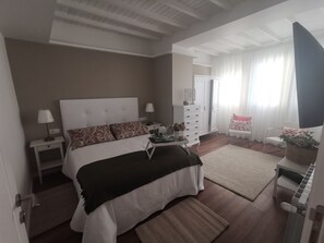 Un dormitorio con cama, mesitas de noche, cómoda, una silla y ventana con cortinas.