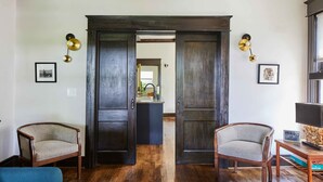 Una habitación con dos puertas de madera, un sofá azul y dos sillas de mimbre.