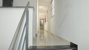 Un pasillo moderno y limpio con piso brillante, baranda metálica y un extintor de incendios colgado en la pared.