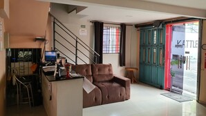 Un vestíbulo de hotel con un sofá, un escritorio con una computadora, una escalera y una puerta que da al exterior.