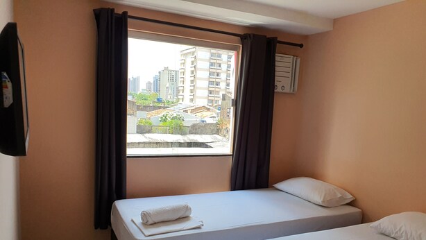Habitación de hotel con dos camas, una ventana con cortinas, aire acondicionado de pared y vista a edificios.