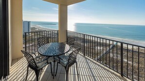 A balcony with a round table and four chairs, overlooking a beach and ocean.