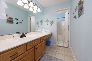 A bathroom with a wooden vanity, white sink, and a mirror with lights. There are towels on the counter and a trash bin next to the door. - 14th floor Two Bedroom at Phoenix VII (Orange Beach)