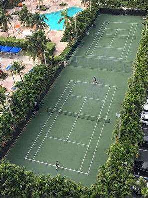 Uma quadra de tênis cercada por palmeiras e uma área de piscina.