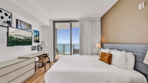 A modern hotel room with a large bed, a desk, and a balcony with a view of the sea. - Luxurious Ocean View 2 Bedroom Escape (Hollywood)
