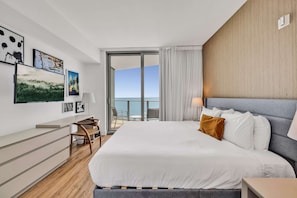 A modern hotel room with a large bed, a desk, and a balcony with a view of the sea. - Luxurious Ocean View 2 Bedroom Escape (Hollywood)