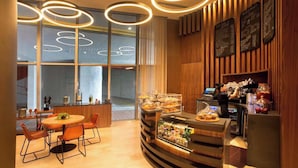 A modern cafe with a wooden interior, a round table with chairs, a counter with a display case, and menu boards. - Luxurious Ocean View 2 Bedroom Escape (Hollywood)