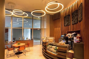 A modern cafe with a wooden interior, a round table with chairs, a counter with a display case, and menu boards. - Luxurious Ocean View 2 Bedroom Escape (Hollywood)