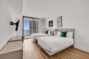 A modern hotel room with two beds, a desk, and a large window offering a city view. - Luxurious Ocean View 2 Bedroom Escape (Hollywood)