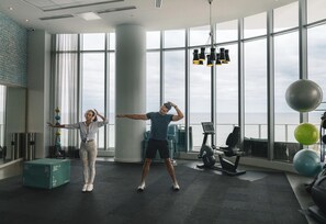 A spacious gym with large windows, exercise equipment, and a view of the sea. - Luxurious Ocean View 2 Bedroom Escape (Hollywood)