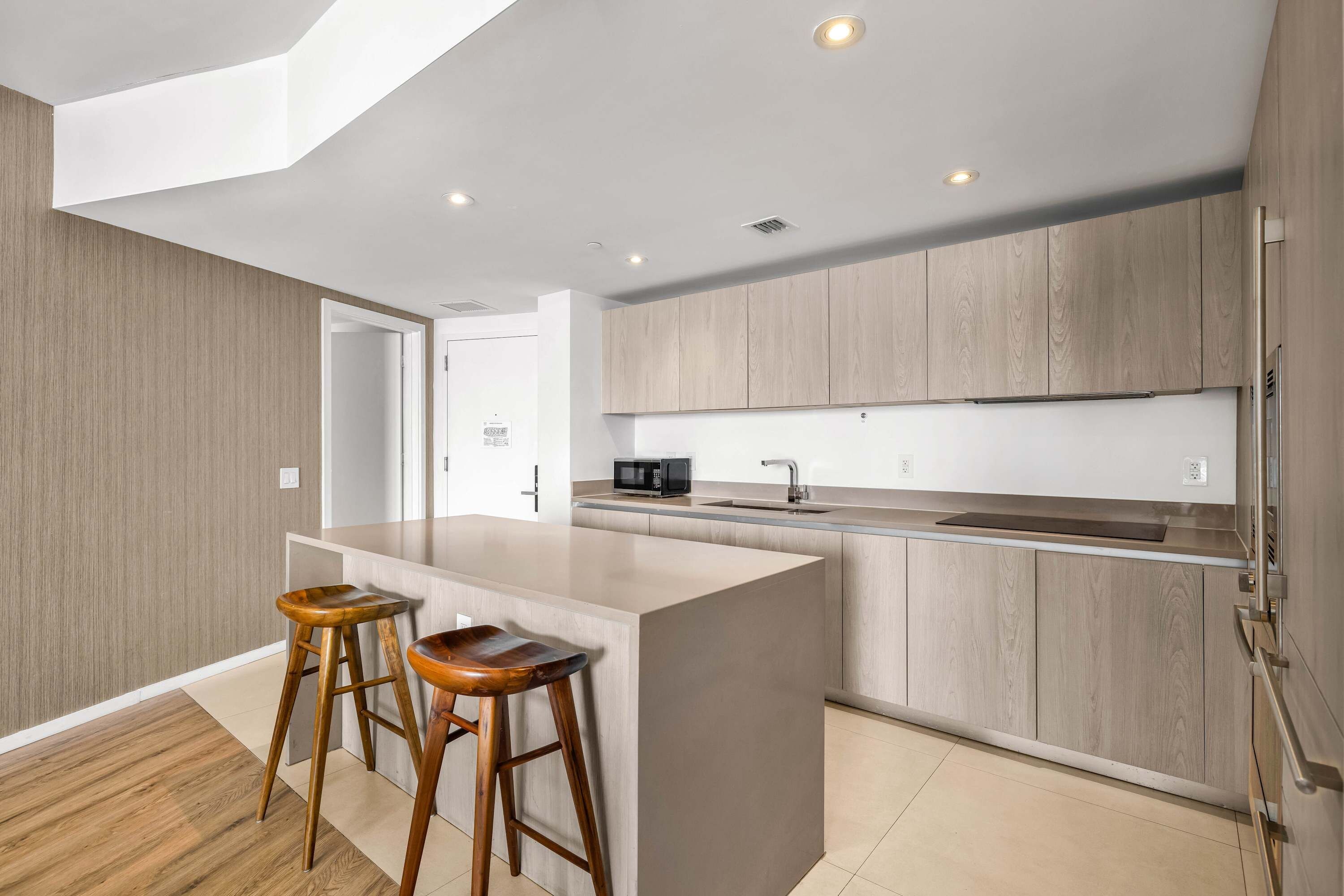 A modern kitchen with a central island, wooden stools, and built-in appliances.