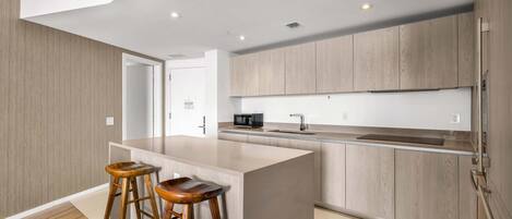 A modern kitchen with a central island, wooden stools, and built-in appliances.