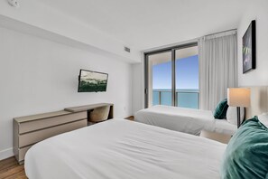 A hotel room with two beds, a desk, a television, and a large window with a view of the sea. - Luxurious Ocean View 2 Bedroom Escape (Hollywood)