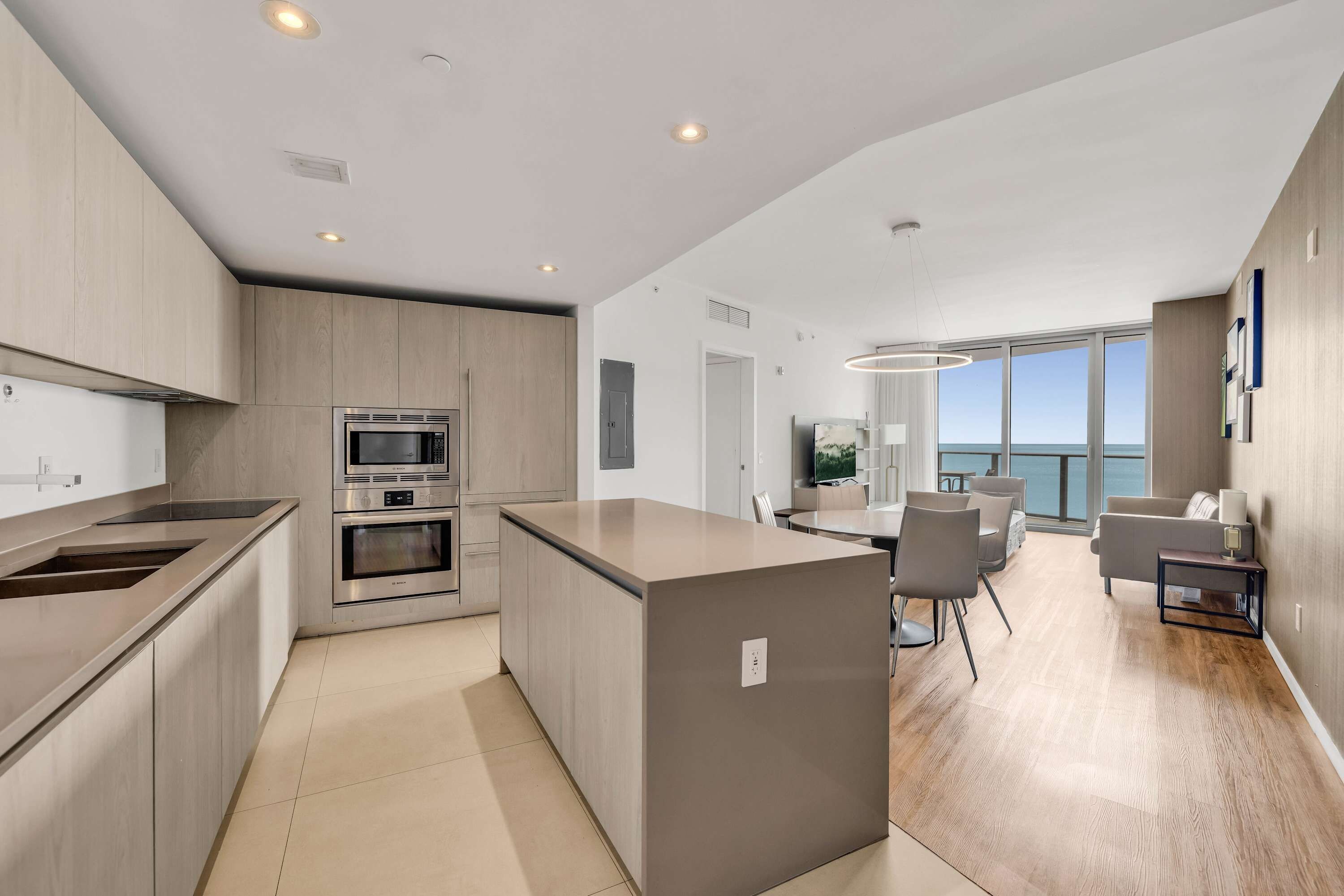 A modern kitchen with built-in appliances, a central island, and a dining area with a view.