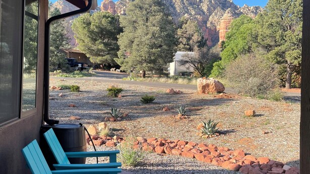 Une terrasse avec un fauteuil Adirondack bleu, un chemin en béton et une vue sur des formations rocheuses rouges et des arbres.