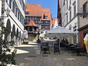 Una calle adoquinada con un café que ofrece mesas al aire libre y una sombrilla blanca.