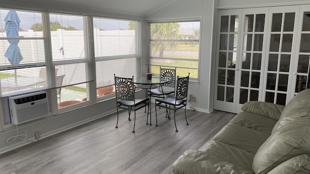 A room with a glass door leading to a patio, a beige sofa, a small table with chairs, and a window with blinds.