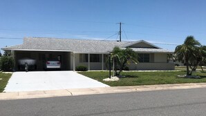 A single-story house with a garage, a covered driveway, and a small lawn with palm trees.
