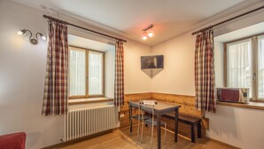 Une pièce avec un plancher en bois, une table avec des chaises, un banc, un radiateur et une fenêtre avec des rideaux.