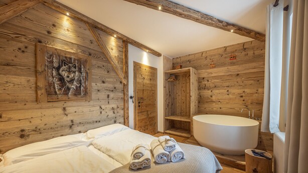 Une chambre à coucher de style cabane en bois, avec un grand lit, une baignoire et une armoire en bois.