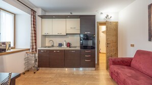 Une cuisine moderne avec des meubles de couleur sombre, un plan de travail en acier inoxydable et un canapé rouge dans l’espace salon.