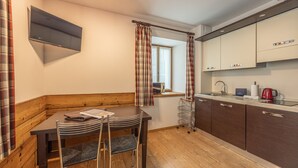 Une cuisine moderne avec des meubles en bois, une table à manger avec des chaises, une fenêtre avec des rideaux et un téléviseur fixé au mur.