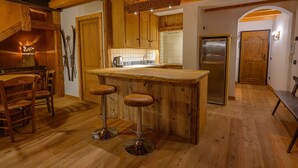 A wooden kitchen with a bar stool area, wooden cabinets, and a refrigerator. - Ciandolada 2 Wellness (Vodo Cadore)