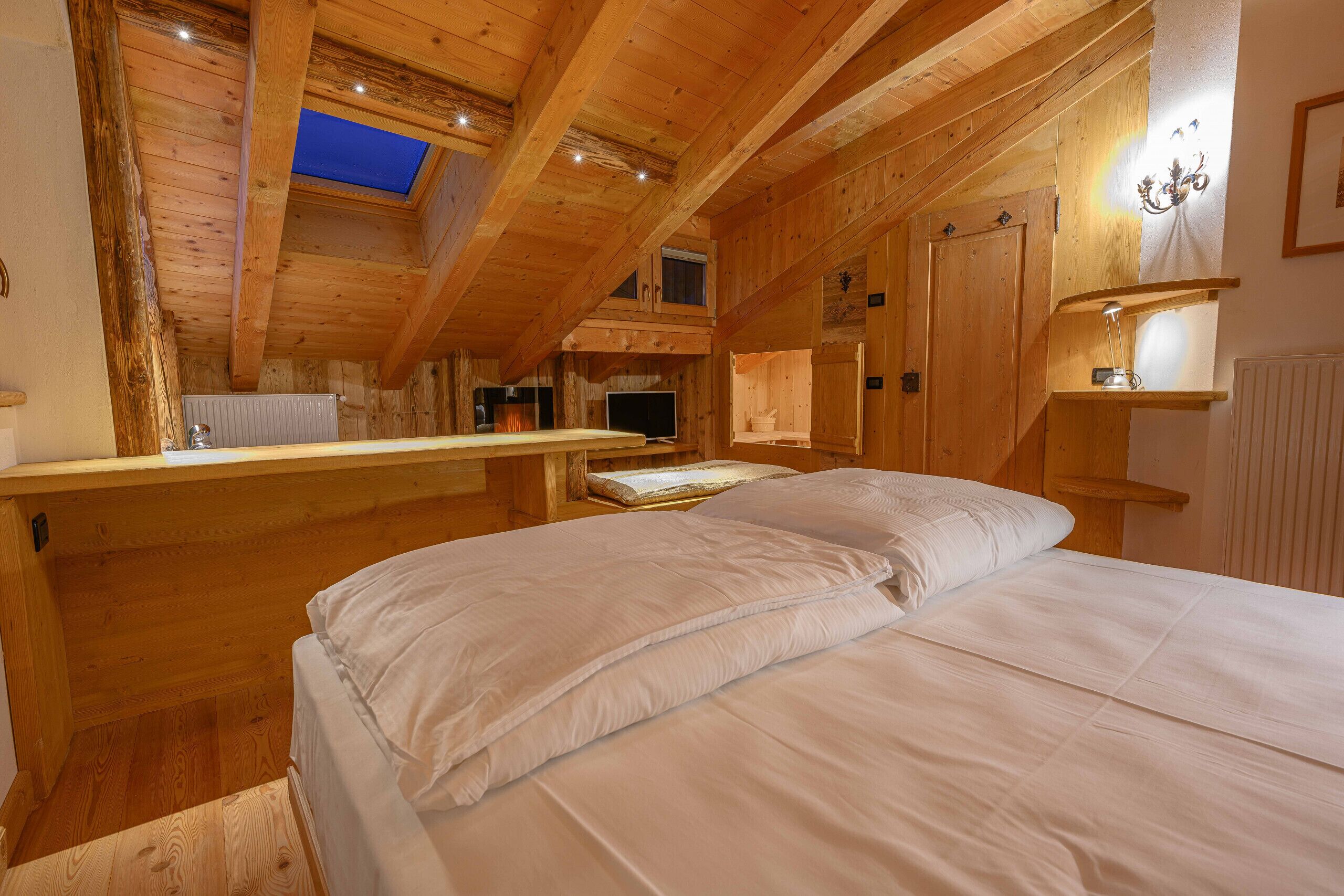A cozy wooden room with a bed, a desk, and a skylight.