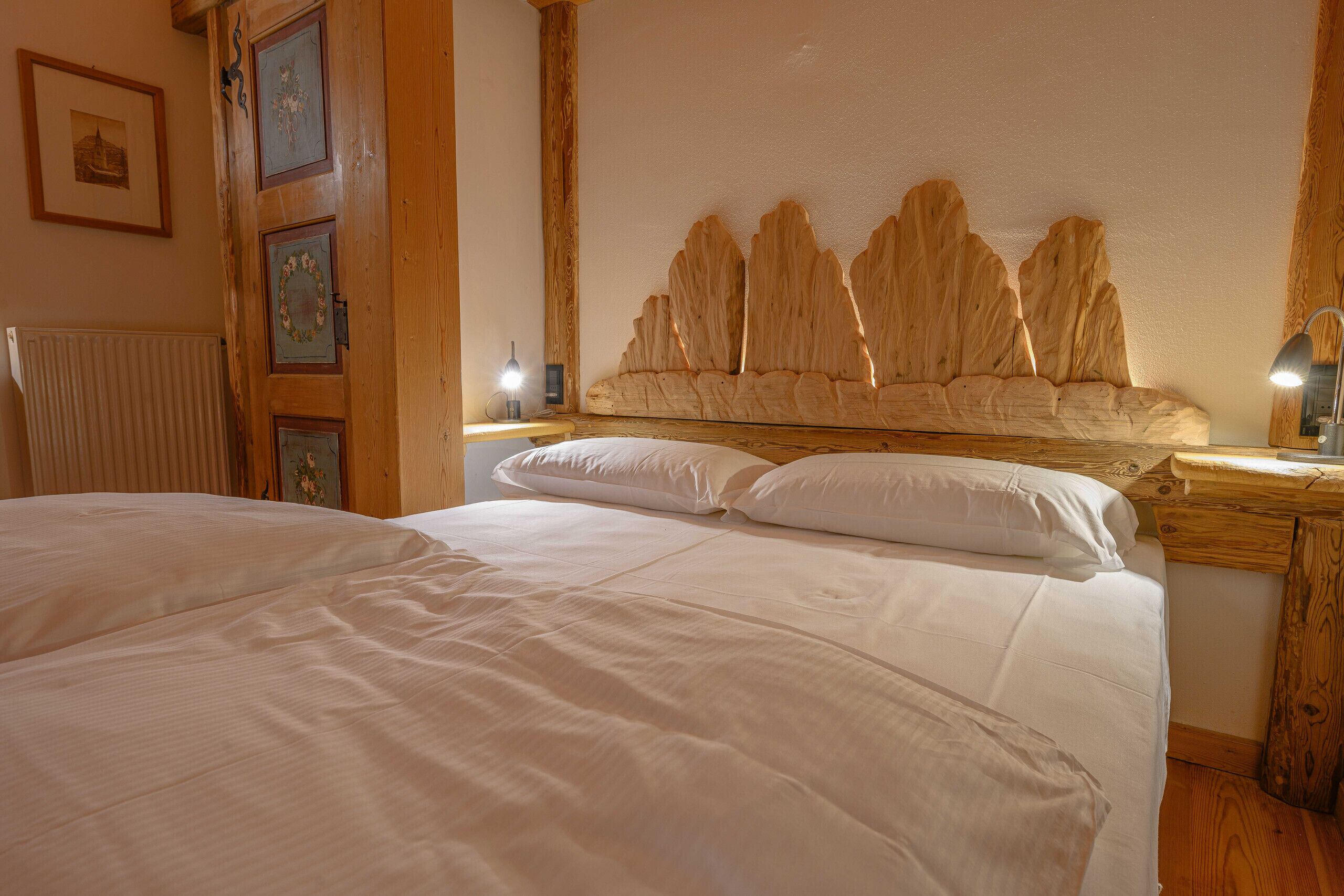 A bedroom with a wooden headboard, a bed with white linens, a nightstand with a lamp, and a framed picture on the wall.