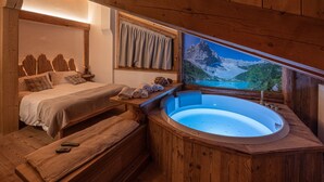 A wooden cabin room with a bed, a bench, a bathtub, and a window with a mountain view. - Ciandolada 2 Wellness (Vodo Cadore)