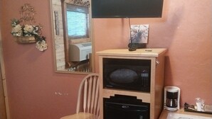 A compact room with a wooden chair, a small black refrigerator, a coffee maker, and a flat-screen TV mounted on the wall. - Liberty Belle Lodge (Aladdin)
