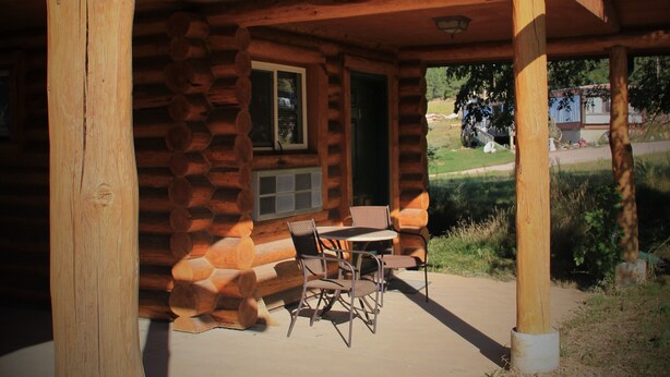 A log cabin with a covered porch, a table, and chairs. - Liberty Belle Lodge (Aladdin)