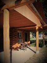 A log cabin with a covered porch, a table, and chairs.